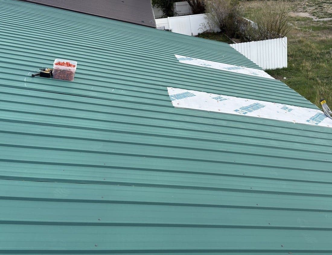 Green metal roof patched with underlayment after wind damage