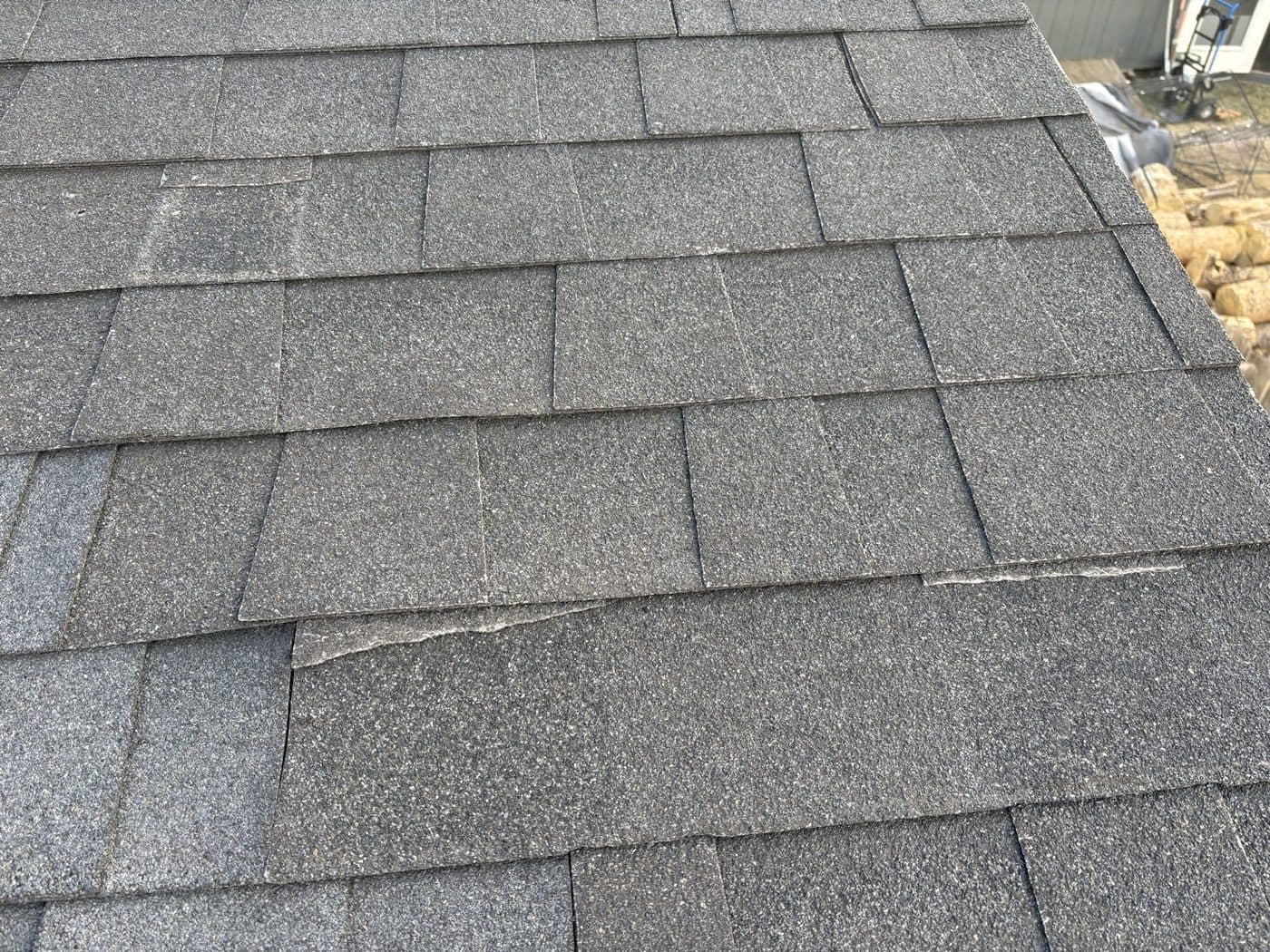Gray asphalt shingles lifted and slipping out of course