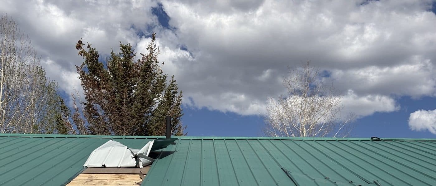 Metal roof with a panel torn off and plywood showing
