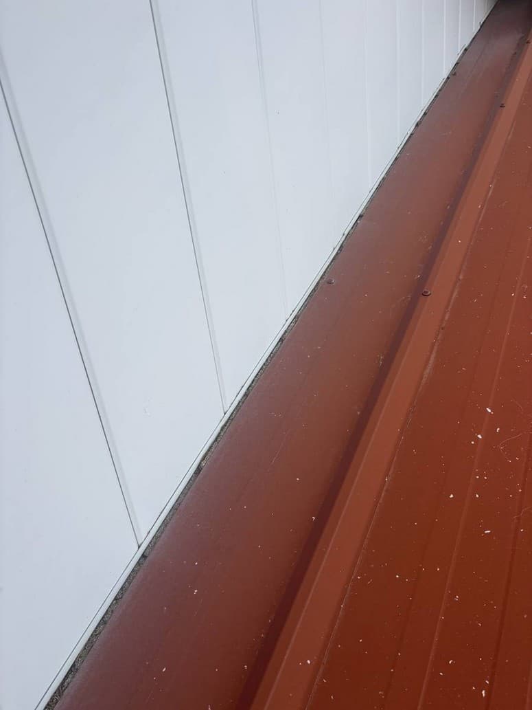 Photo 2 — Roof run to the white wall. No step flashing. No wall trim.